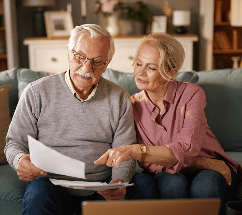 Elderly couple reviewing documents on couch.