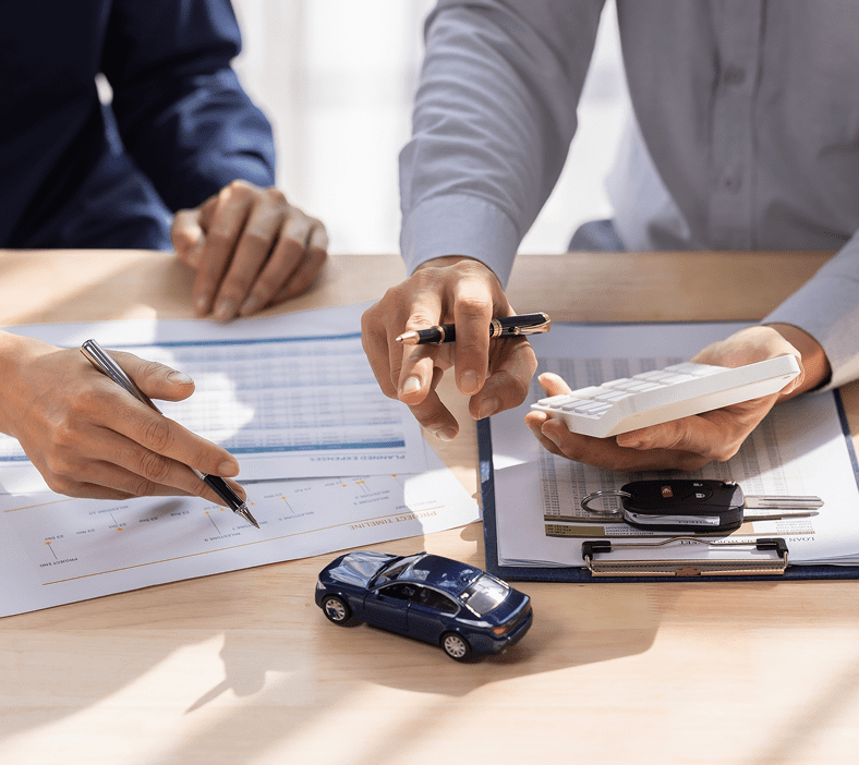 Hands signing documents with calculator and car.