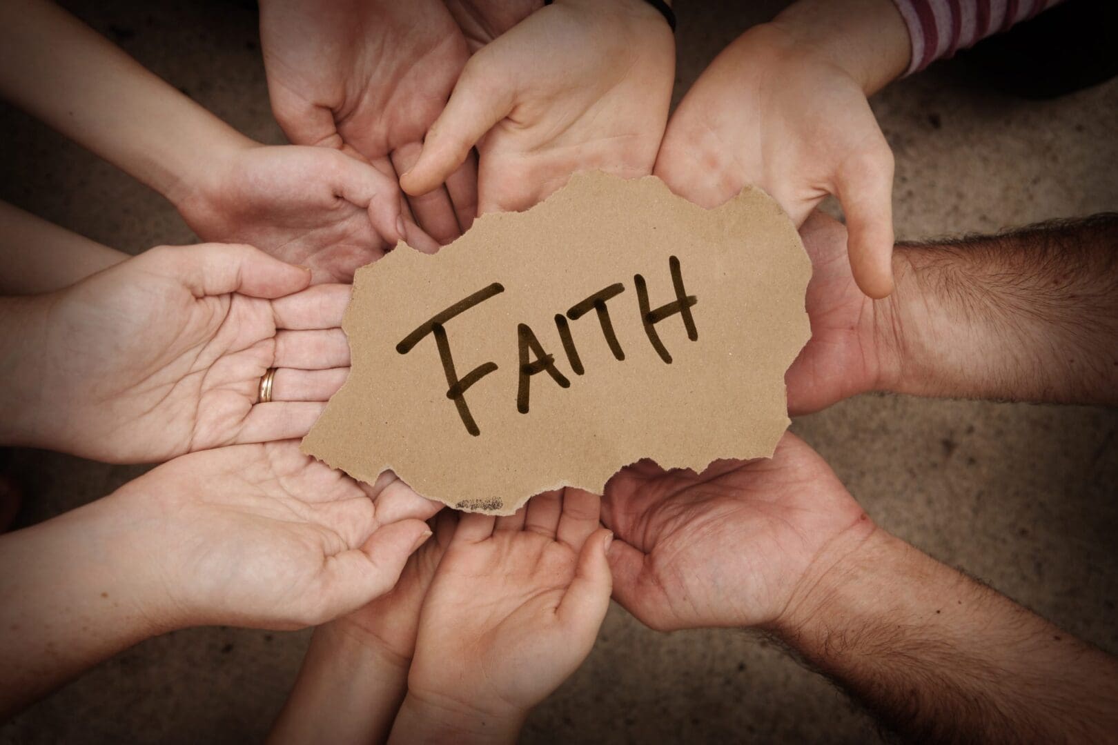 Hands holding "Faith" sign together.