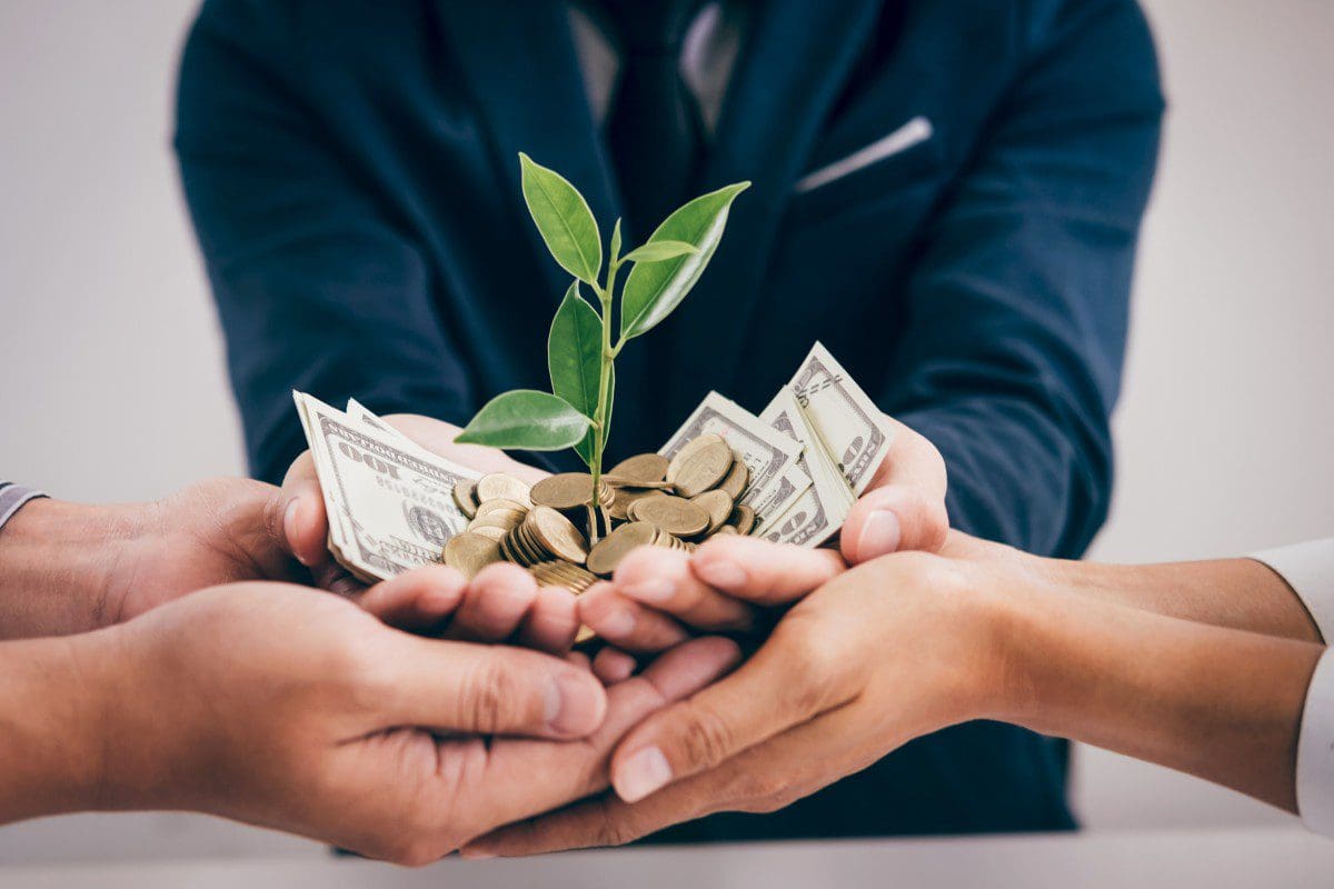 Hands holding plant, coins, and dollar bills.