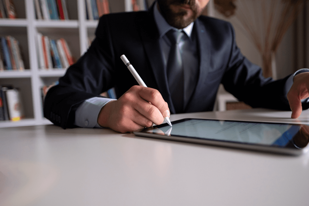 Man in suit writing on tablet in a professional setting.